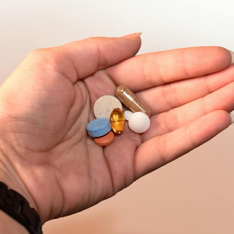 A close-up image of a human hand holding assorted pills, showcasing diverse colors and shapes.
