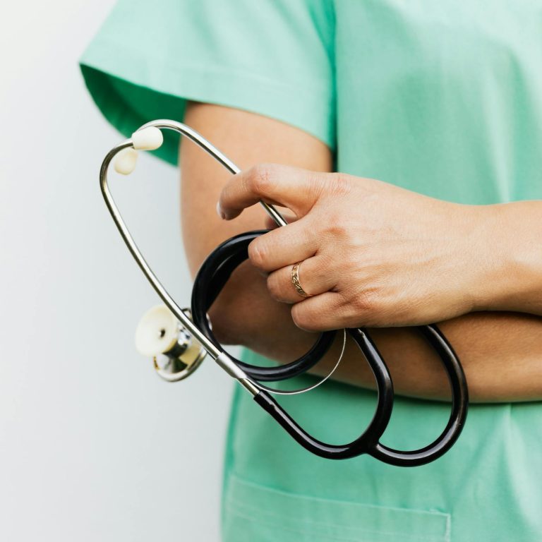 Close-up of a healthcare professional in scrubs holding a stethoscope.