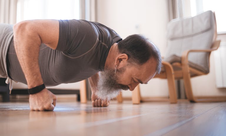 Elderly man exercising indoors with push-ups on a wooden floor for fitness.