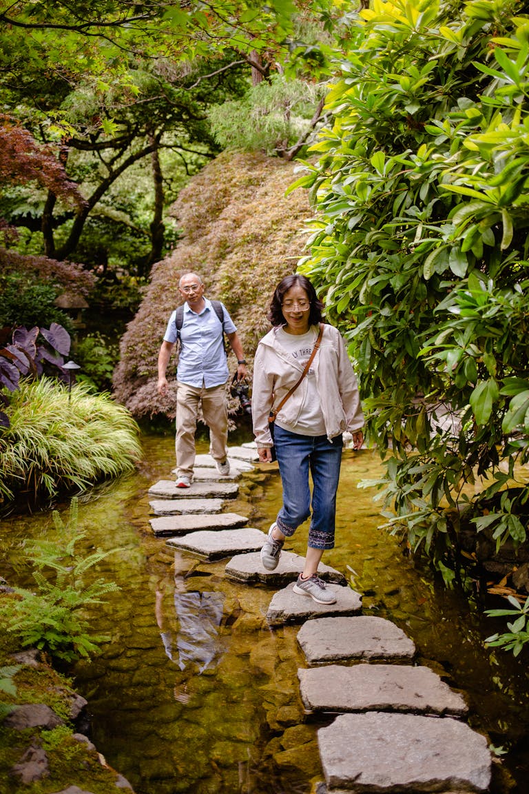 Senior couple exploring a lush garden, stepping on stones over a serene water feature.